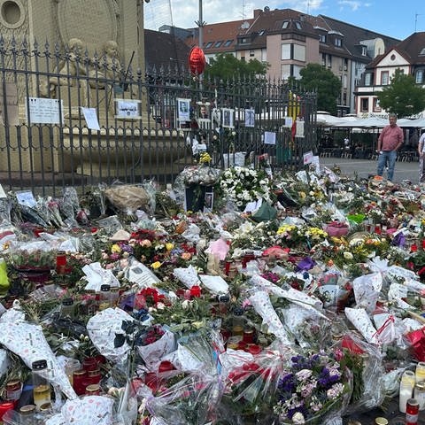 Blumen und Blumensträuße vor Brunnen auf Marktplatz Mannheim, Frau steht daneben und trauert
