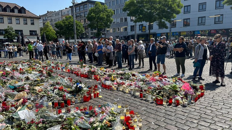 Menschen auf Marktplatz Mannheim vor Blumen und Kerzen auf dem Boden