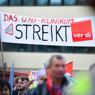 Streikende Beschäftigte halten bei einer Kundgebung vor dem Universitätsklinikum Heidelberg ein Transparent mit der Aufschrift «Das Uni-Klinikum streikt» in die Höhe