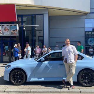 Ein Autposer steht in Mannheim vor seinem blauen Wagen