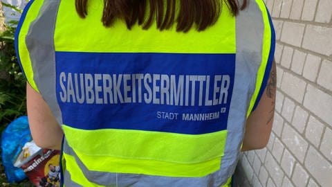 Die Mitarbeiter tragen eine gelb-blaue Weste, auf denen steht: Sauberkeitsermittler Stadt Mannheim