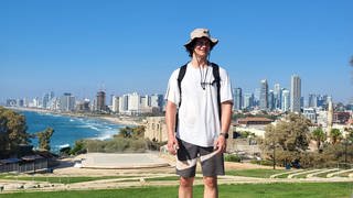 Benedikt Jahn steht vor der Skyline von Tel Aviv am Meer