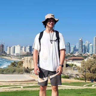 Benedikt Jahn steht vor der Skyline von Tel Aviv am Meer