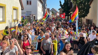 Hunderte Menschen gehen mit Regenbogen-Flaggen durch eine Straße in Ketsch.