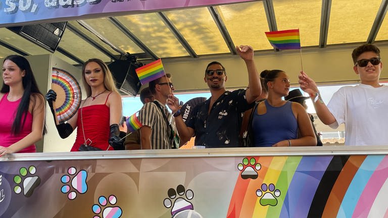 Menschen feiern und tanzen mit Regenbogen-Flaggen in einem Umzugswagen in Ketsch bei der Dorfpride