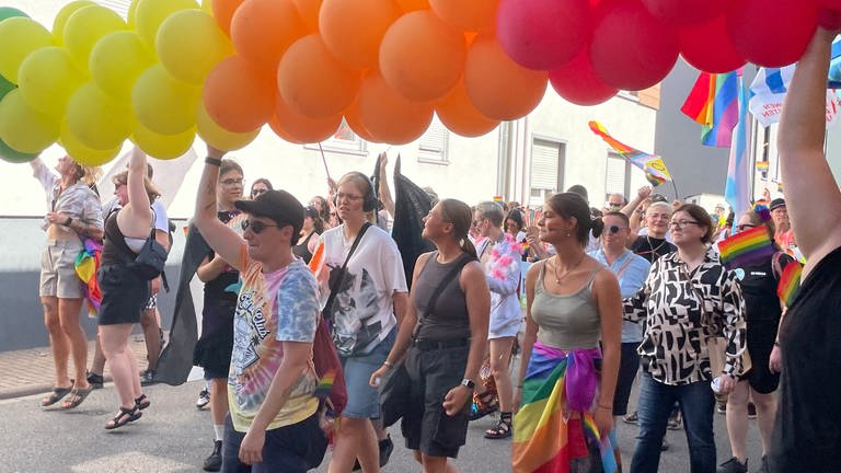 Menschen bei einer Pride-Demonstration mit bunten Luftballons und Regenbogen-Flaggen in Ketsch.