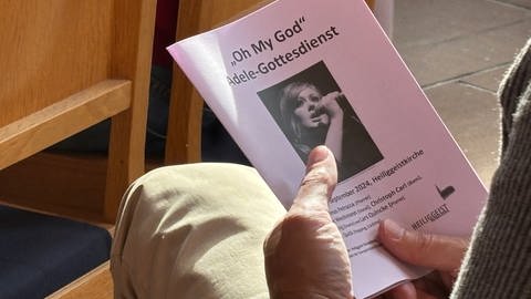 Ein Kirchenbesucher hat das Programmheft des "Adele"-Gottesdienstes in der Hand.