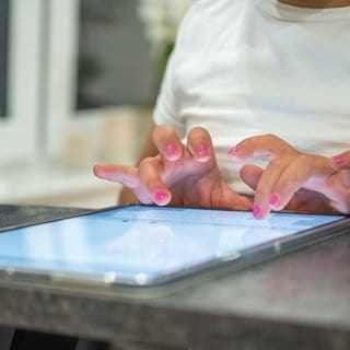 Ein Mädchen sitzt an einem Tabletcomputer und tippt.