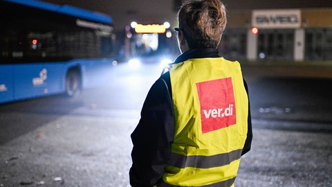 Eine Streikende steht bei einem Warnstreik der Gewerkschaft ver.di am Gelände der SWEG vor einem abfahrenden Bus.