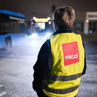 Eine Streikende steht bei einem Warnstreik der Gewerkschaft ver.di am Gelände der SWEG vor einem abfahrenden Bus.