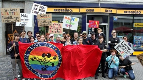 Menschen protestieren beim Christopher Street Day für queere Rechte. Sie haben Schilder und Plakate.