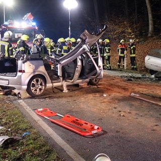 Feuerwehrleute stehen hinter den Trümmern von zwei Autos, die bei Gauangelloch (Rhein-Neckar-Kreis) zusammengestoßen sind.