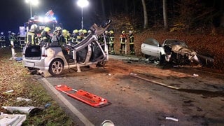 Feuerwehrleute stehen hinter den Trümmern von zwei Autos, die bei Gauangelloch (Rhein-Neckar-Kreis) zusammengestoßen sind.