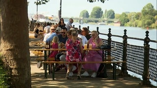 Menschen sitzen im Sommer an Tischen mit Blick auf den Neckar in Heidelberg