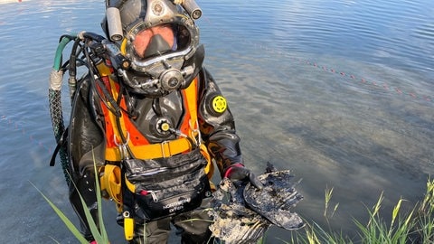 Ein Taucher im knietiefen Wasser mit zerborstener Öl-Dose in der Hand.