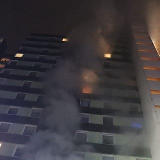 In einem 14-stöckigen Hochhaus im Heidelberger Stadtteil Emmertsgrund brennt es. Rauch steigt aus einem Fenster.