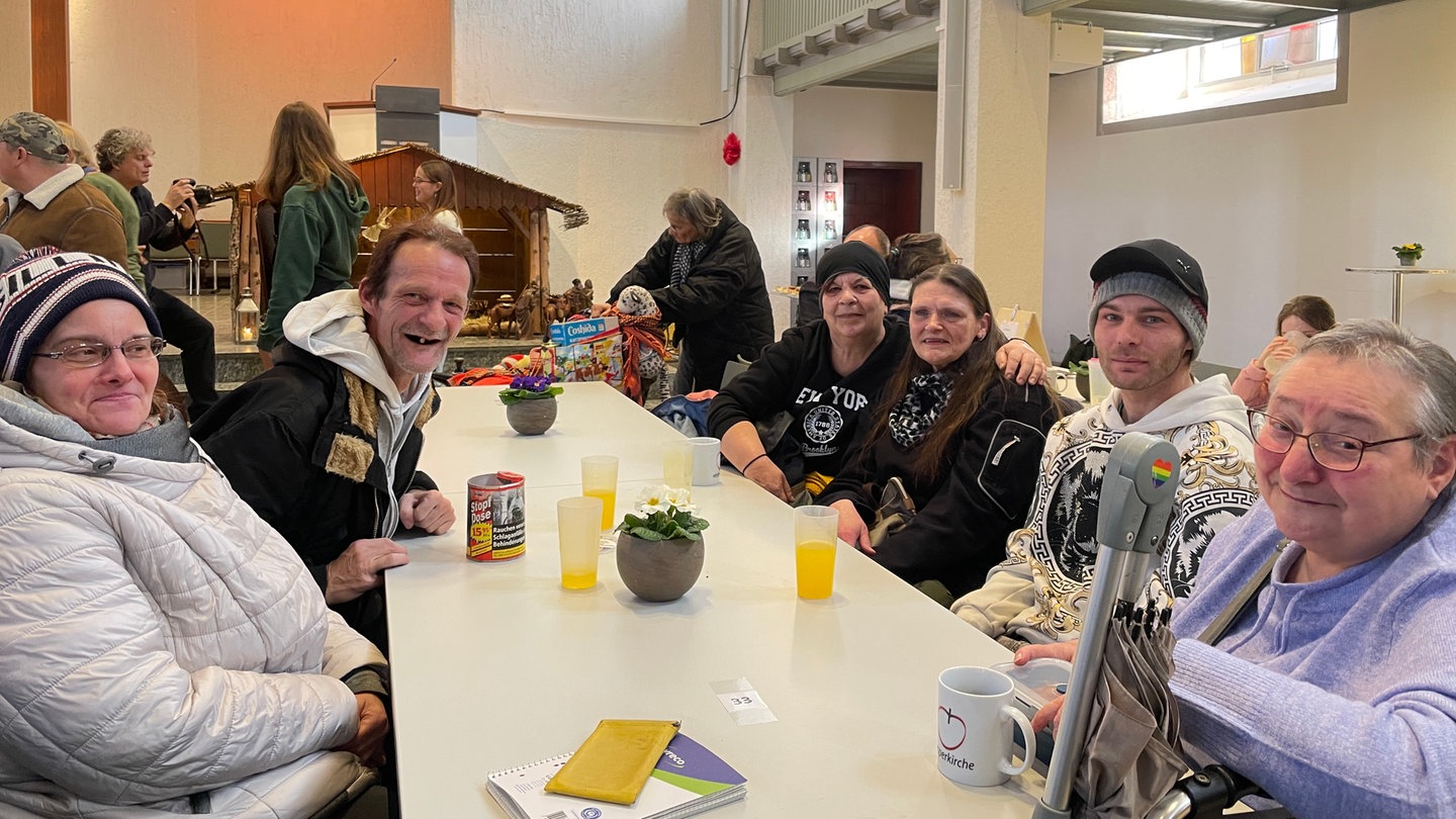 Eine große Tafel mit unterschiedlichen Menschen. Sie sind alle zu Gast in der Vesperkirche und lächeln in die Kamera.