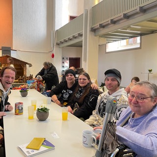 Eine große Tafel mit unterschiedlichen Menschen. Sie sind alle zu Gast in der Vesperkirche und lächeln in die Kamera.