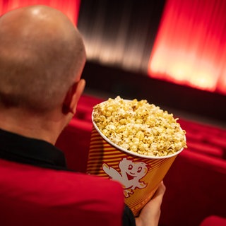 Eine Person sitzt mit einem Snack in einem Kino (Symbolbild).