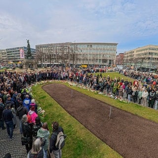 Menschen stehen bei dem interreligiösen Gebet auf dem Paradeplatz in Mannheim zusammen.