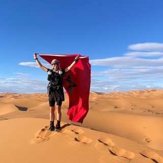 Nach ihrem Lauf durch die Sahara hält die Wüstenläuferin Tanja Braun siegreich die marokkanische Flagge in die Höhe.