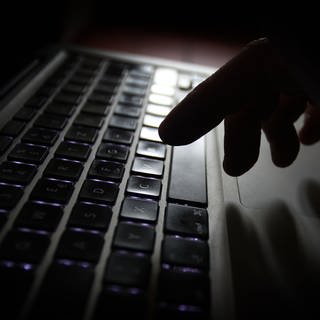 Eine Hand an einer Laptop-Tastatur. Es geht dabei um Cyber-Kriminalität.