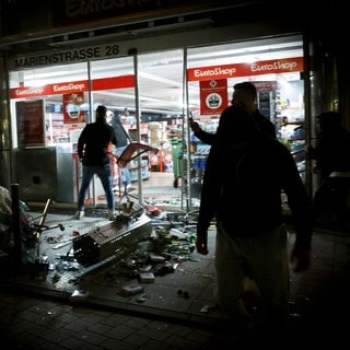 Menschen stehen vor einem geplünderten Geschäft in der Marienstraße.