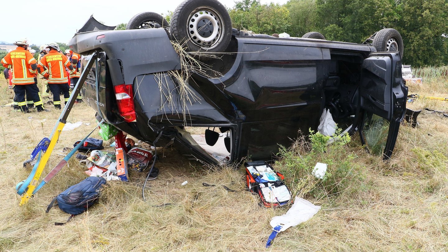 Einsatzkräfte der Feuerwehr stehen neben einem verunfallten Fahrzeug, das auf dem Dach liegt. Bei einem Unfall auf der Autobahn 81 bei Stuttgart sind sechs Menschen verletzt worden. Ein Transporter mit sechs Insassen sei am Übergang der Bundesstraße 10 auf die A81 aus bislang unklarer Ursache am Freitag von der Fahrbahn abgekommen, sagte eine Sprecherin der Polizei. Der Wagen überschlug sich und blieb neben der Fahrbahn stehen.