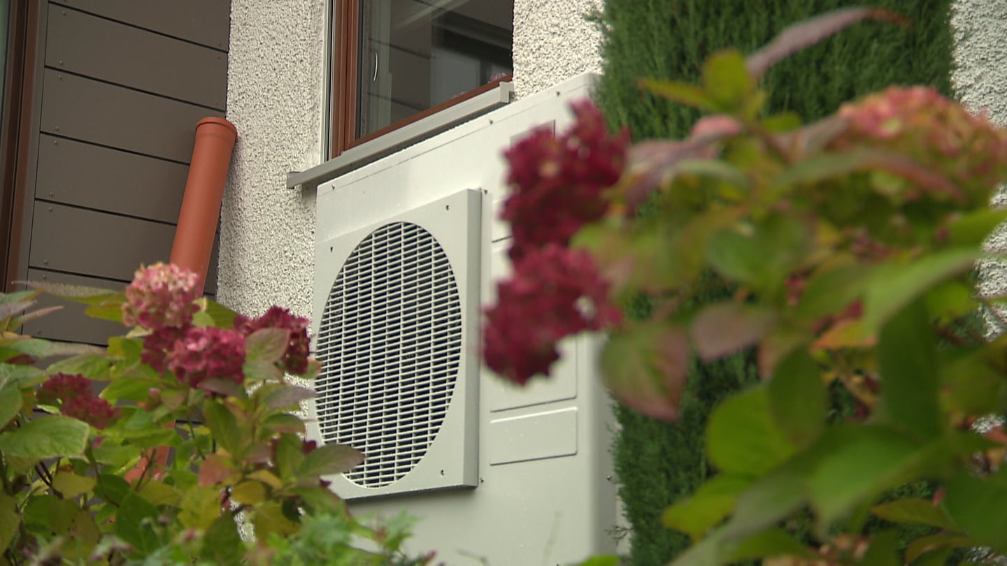 Eine Wärmepumpe steht an einer Hauswand. Sie soll aus der Luft die Wärme absaugen und damit das Haus heizen.