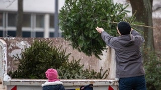 Ein Mann wirft vor seinen Kindern einen alten Weihnachtsbaum in einen Container.