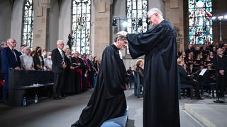 Ernst-Wilhelm Gohl (kniend) wird von seinem Vorgänger Frank Otfried July (rechts) in der Stuttgarter Stiftskirche in sein neues Amt als neuer evangelischer Landesbischof für Württemberg eingeführt.