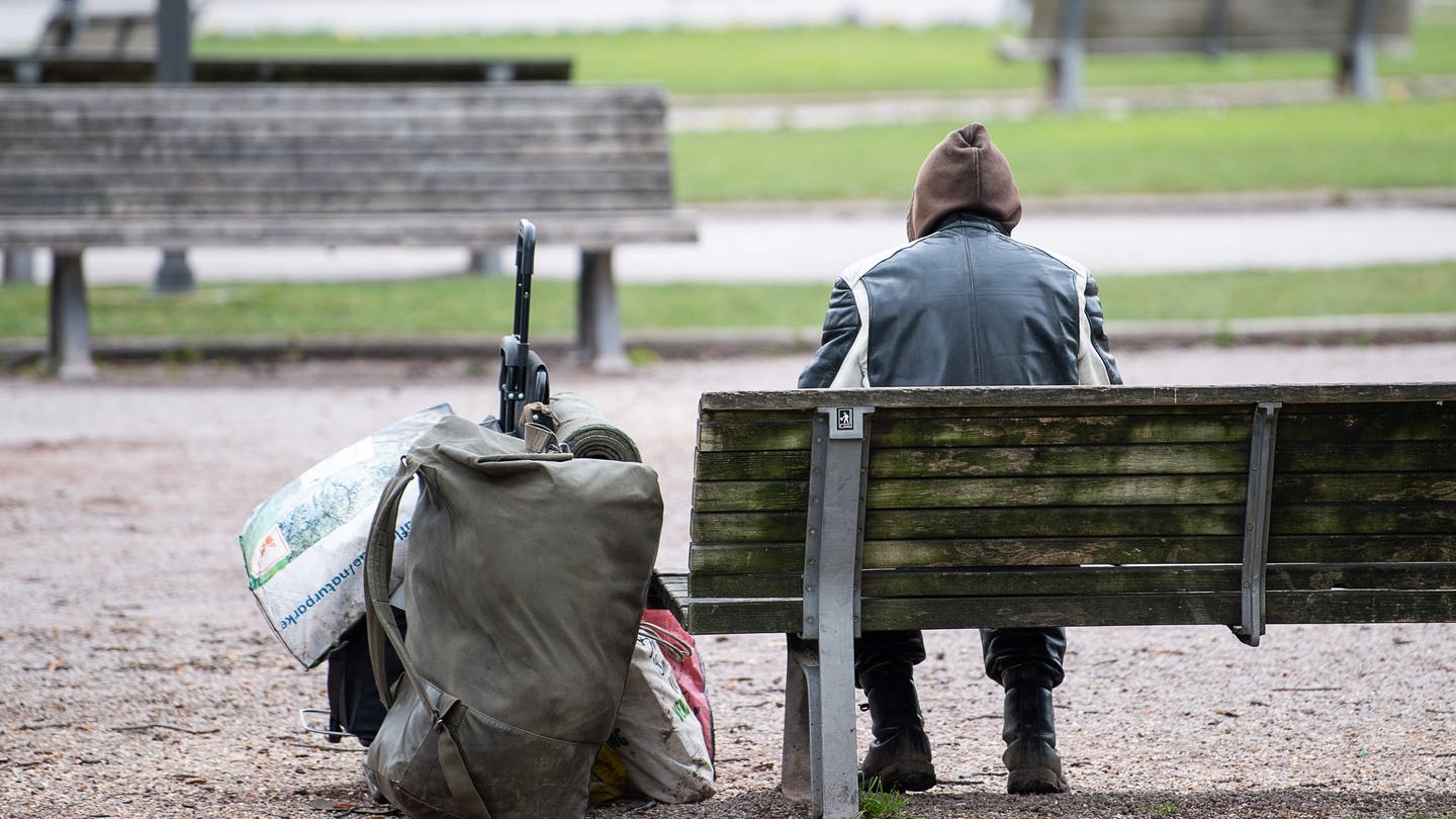 Ein Mann sitzt mit seinen Habseligkeiten auf einer Parkbank.