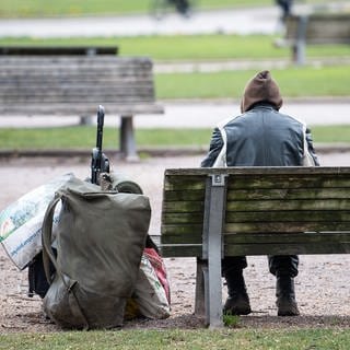 Ein Mann sitzt mit seinen Habseligkeiten auf einer Parkbank.