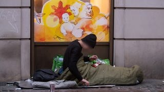 Ein obdachloser Mann liegt in seinem Schlafsack vor einer Drogerie in der Kaiserstraße im Bahnhofsviertel von Frankfurt.