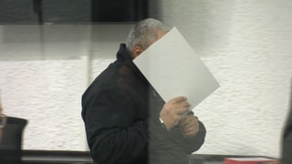 Der Angeklagte betritt mit  einer Mappe vor dem Gesicht den Gerichtssaal am Landgericht Stuttgart. Er soll im vergangenen Sommer einen Senior in Ludwigsburg mit einem Messer niedergestochen und getötet haben.