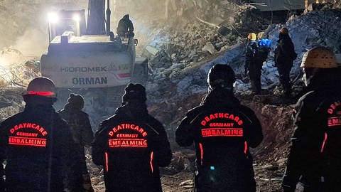 Vier Helfer stehen nachts vor den Trümmern.