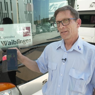 Busfahrer steht vor dem Expressbus nach Waiblingen und zeigt auf dem Handy ein Foto seiner Frau