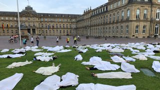 Rund 200 Personen haben sich mit Leintüchern vor das Neue Schloss in Stuttgart gelegt, um am Weltflüchtlingstag an die Toten bei einem Schiffsunglück vor Griechenland zu erinnern.