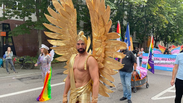 Ein Mann demonstriert mit goldenen Flügeln bei der Demo des Christopher Street Days 2023.