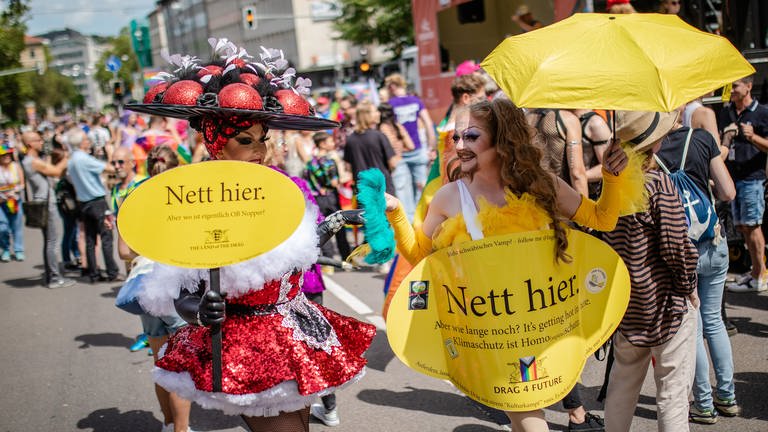 Zwei Teilnehmer beim Christopher Street Day in Stuttgart tragen Plakate vor sich her im Stil der "Nett hier"-Kampagne der Landesregierung, allerdings mit Botschaften an den Stuttgarter Oberbürgermeister und zum Klimaschutz.