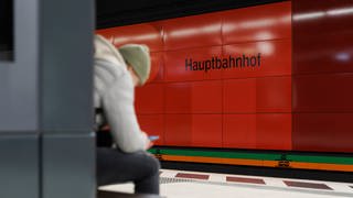 Am Stuttgarter Hauptbahnhof sitzt ein junger Mann mit seinem Handy und wartet auf einen Zug.