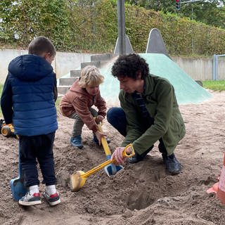 Florian Treßelt sitzt in einem Sandkasten mit Kindern. Der 35-Jährige lässt sich gerade zum Pädagogen umschulen.