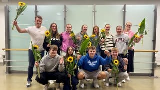 Schülerinnen und Schüler zusammen mit ihren Lehrkräften halten Sonnenblumen hoch. Sie sind kurz zuvor auf dem Flughafen Stuttgart angekommen.