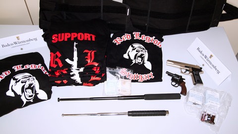 Auf einem Tisch liegen Waffen und T-Shirts der Red Legion.