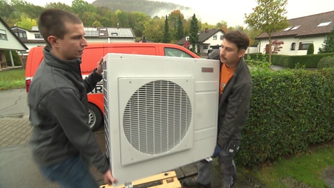 Christian Bühler (links) und sein Kollege transportieren die Wärmepumpe an die richtige Position an der Hauswand.