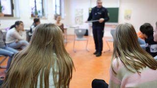 Polizist gibt Unterricht in einer Schulklasse (Symbolbild)
