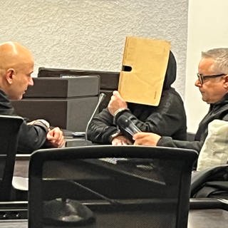 Der Angeklagte hält einen beige-farbenen Ordner vor sein Gesicht - beim Prozessauftakt im Landgericht Stuttgart.