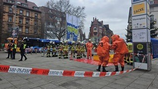 Großeinsatz der Feuerwehr am Marienplatz in Stuttgart: Auf der Treppe in die Stadtbahn-Unterführung hinunter wurde eine verdächtige Flüssigkeit gefunden. Feuerwehrleute in orangen Anzügen stehen auf dem Platz.