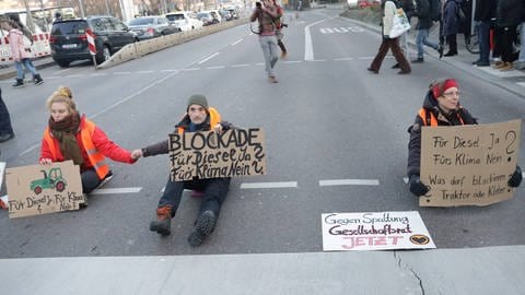 Klima-Protest: Aktivisten der Letzten Generation haben in Stuttgart eine Straße blockiert. Auf Schilder hatten sie Traktoren gemalt und geschrieben: "Blockade für Diesel Ja? Fürs Klima Nein?"