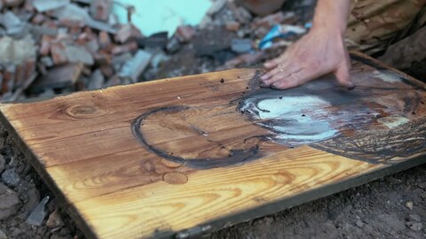 Die Hand von Oleksandr Klymenko wandert über das Holz und trägt Farbe auf. Um die Ikone verteilt liegen Trümmer und Schutt.